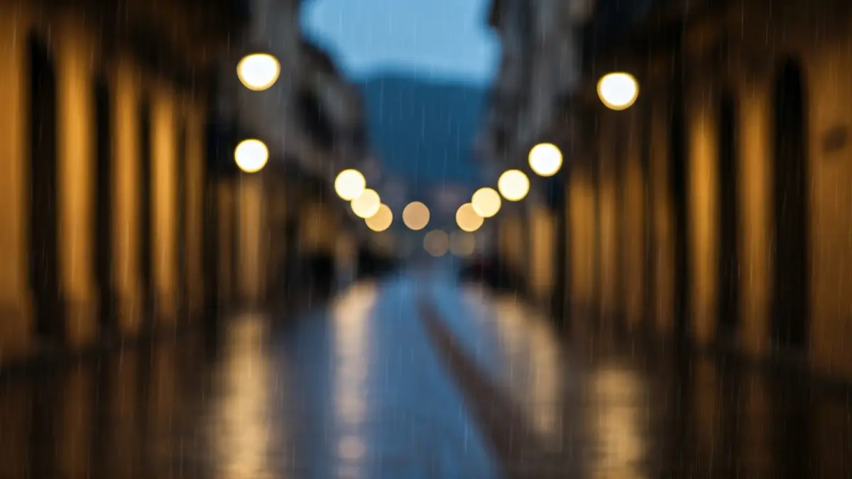 Imagen genérica de lluvia en una ciudad mediterránea, con edificios y farolas borrosas.