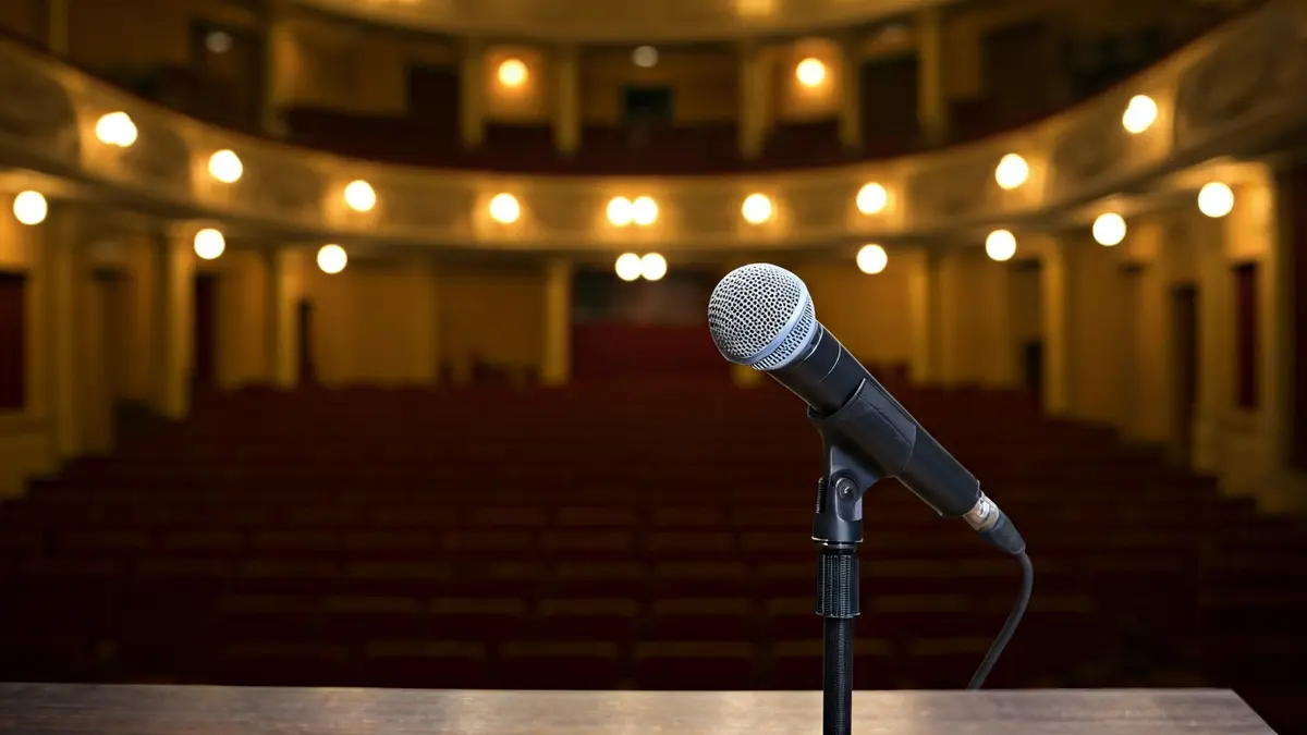 Generic image of a microphone on a podium in an empty theater, with warm lighting.