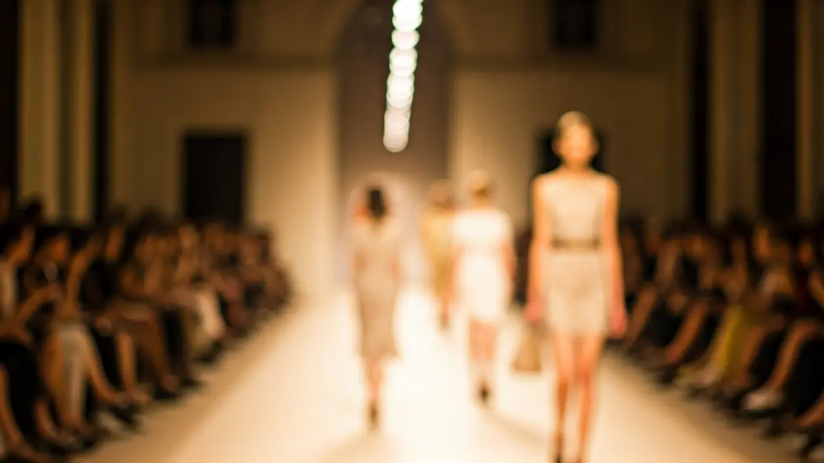 Imagen genérica de una pasarela de moda con iluminación cálida y figuras borrosas de modelos.