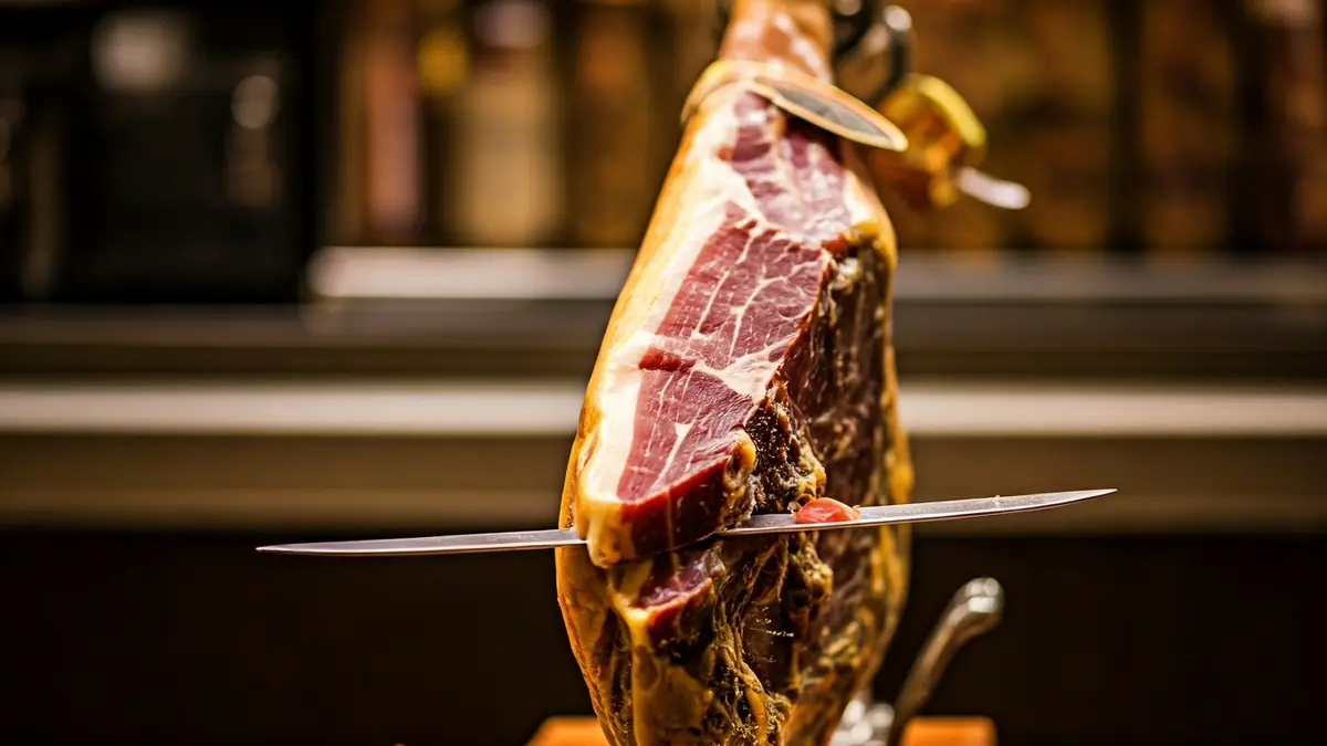 Imagen de un jamón curado siendo cortado en finas lonchas.