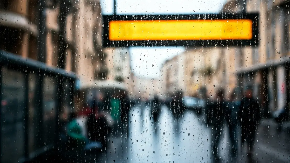 Imagen genérica de una parada de autobús con un horario borroso y personas esperando, bajo la lluvia.