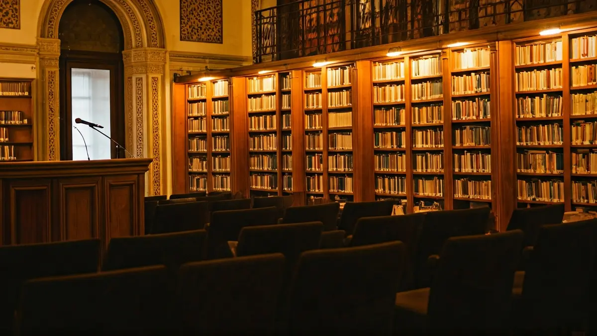 Imagen genérica de una biblioteca con un podio y sillas, en un ambiente cálido.