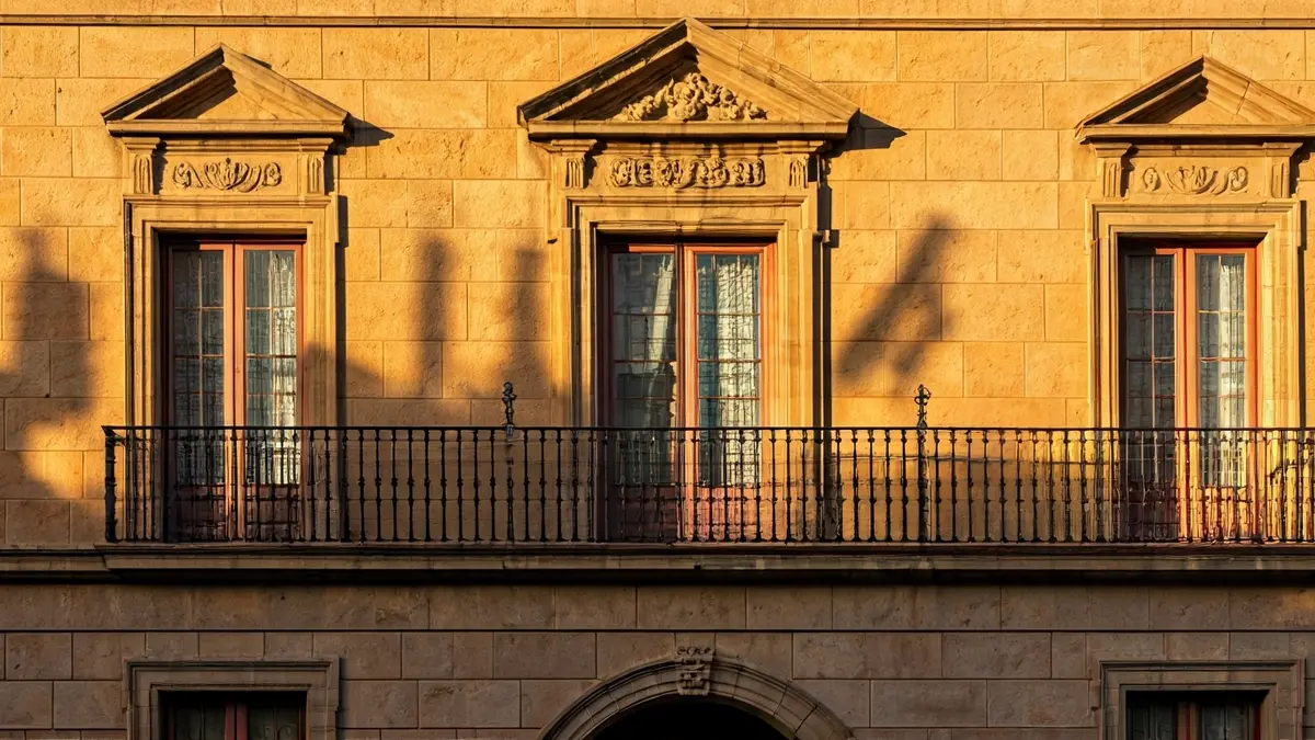 Fachada de un ayuntamiento andaluz con balcón y rejas de hierro, bajo la luz del sol de la tarde.