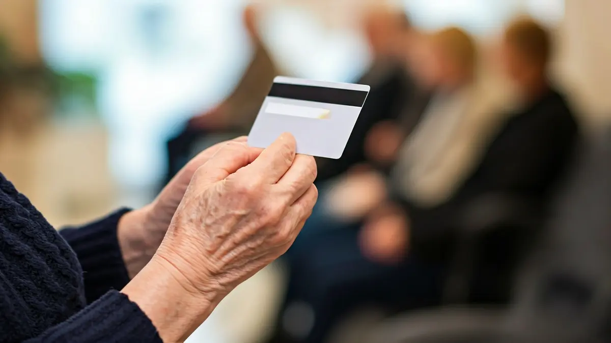 Imagen genérica de una persona mayor sosteniendo una tarjeta, con un fondo borroso de una clínica dental.