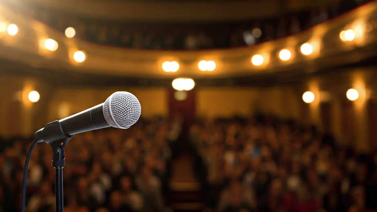 Generic image of a microphone on an empty theater stage with warm lighting.