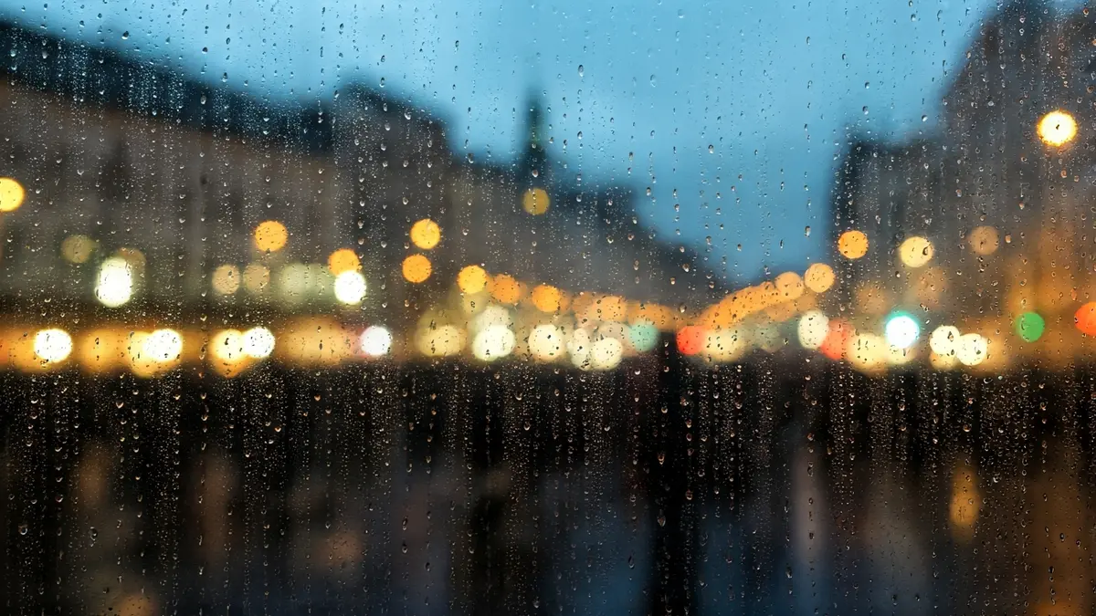 Imagen genérica de lluvia cayendo sobre un cristal, con luces de ciudad borrosas al fondo.