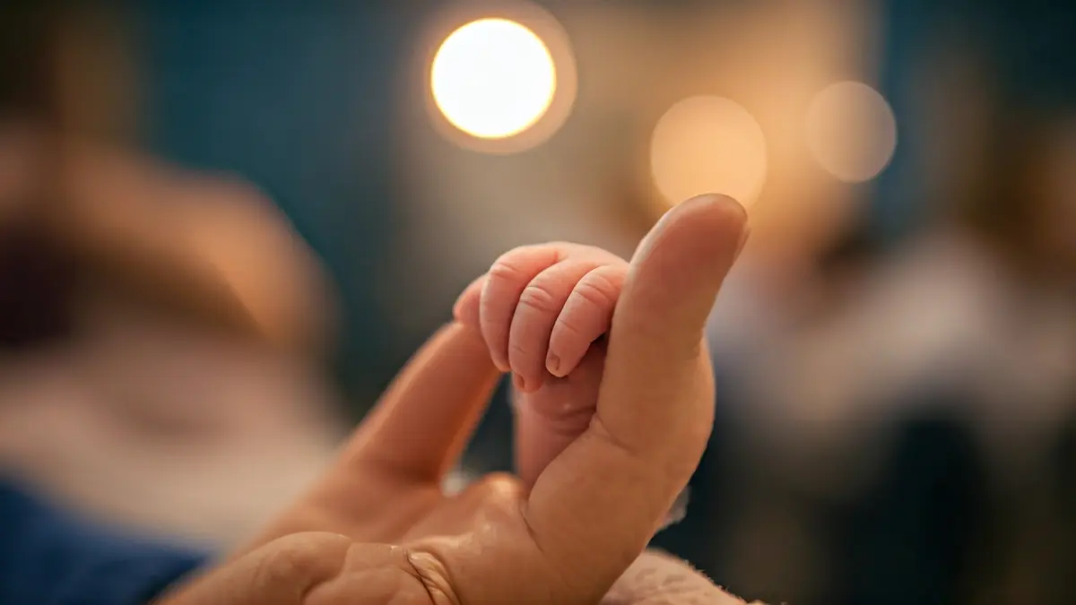 Image of a newborn baby holding an adult's finger, symbolizing hope.
