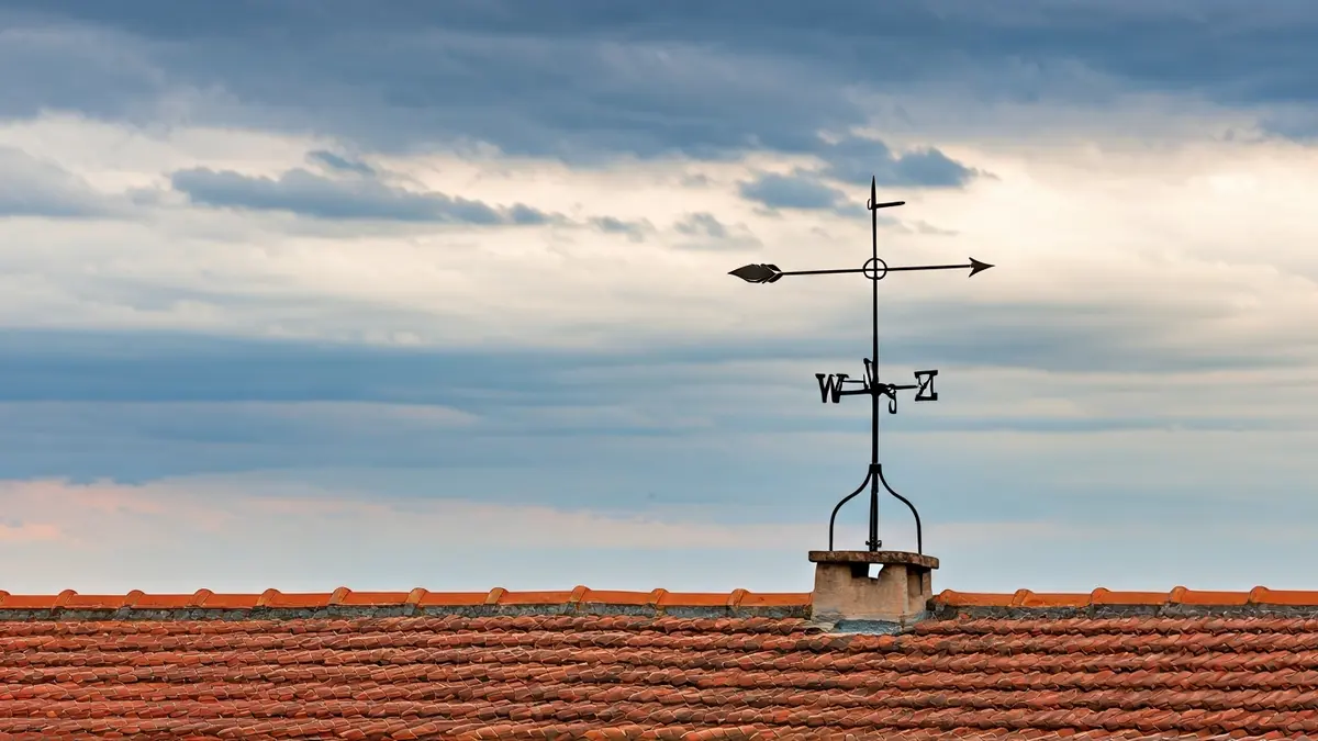 Generic image of a weather vane on a rooftop under a cloudy sky in a coastal town.