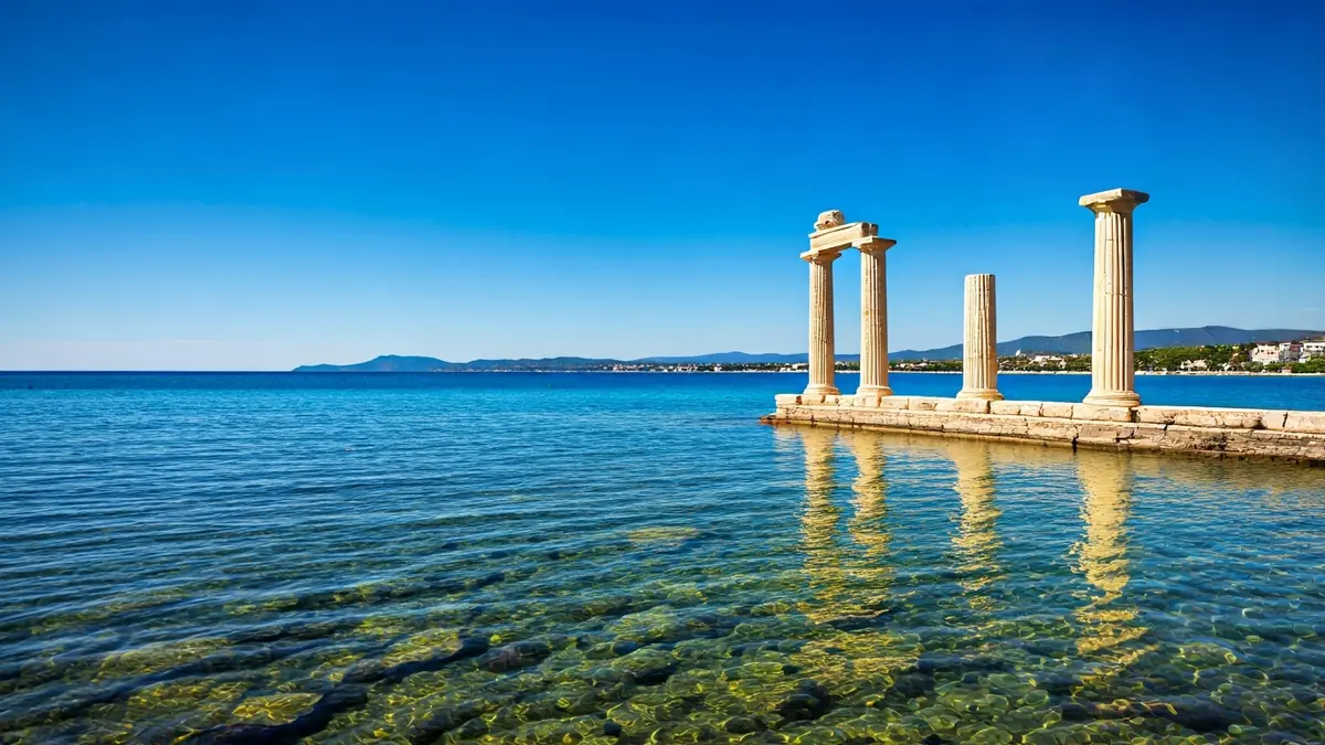 Image of ancient temple ruins, partially submerged in water, with a blue sky and Mediterranean coastline in the background.
