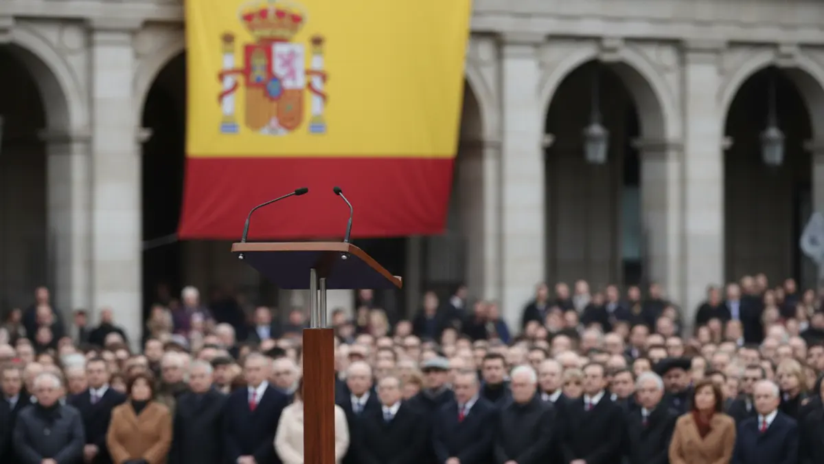 Image of an official ceremony with a microphone and a Spanish flag in the background.