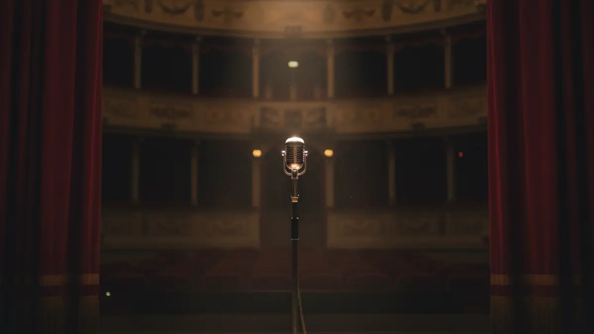 Generic image of a classic theater stage with a microphone and red curtains.