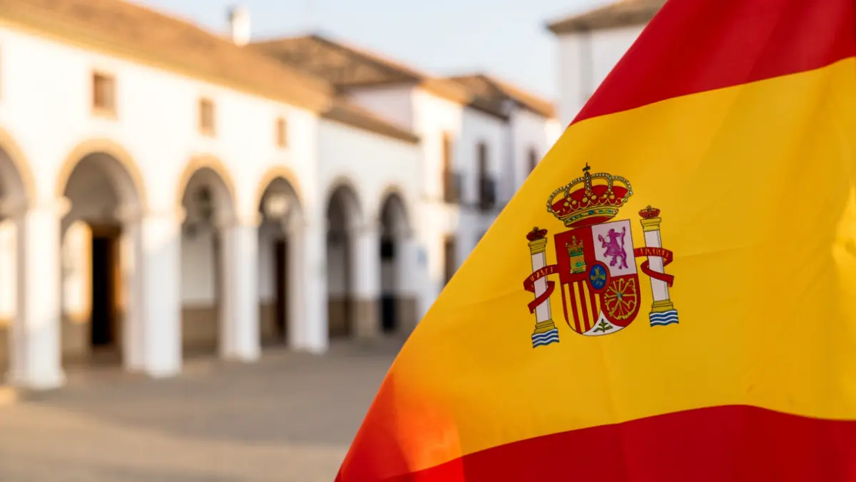 Spanish flag waving with a blurred background of an Andalusian square.