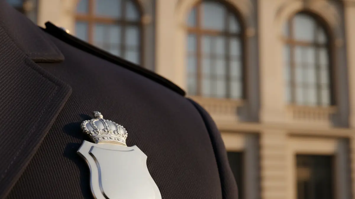 Generic image of a local police officer, with a badge on the uniform and a municipal building in the background.