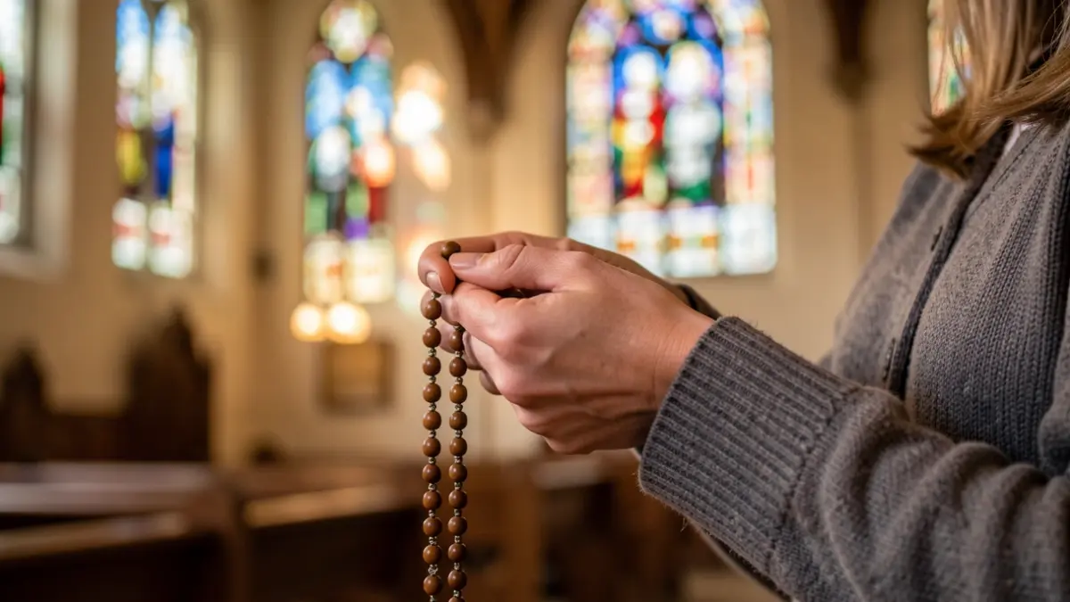 Close-up of a woman's hands holding a rosary, with a blurred background of a church interior and stained glass windows, warm, devotional lighting.