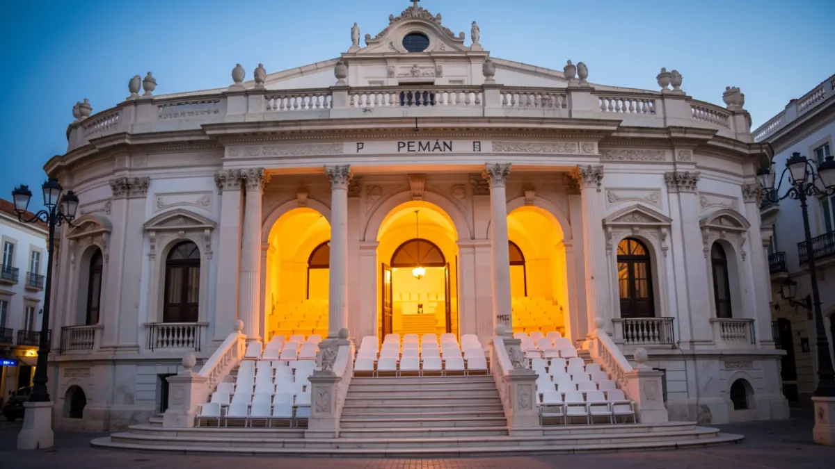 Fachada del Teatro Pemán en Cádiz al atardecer, con luces encendidas y el graderío visible.