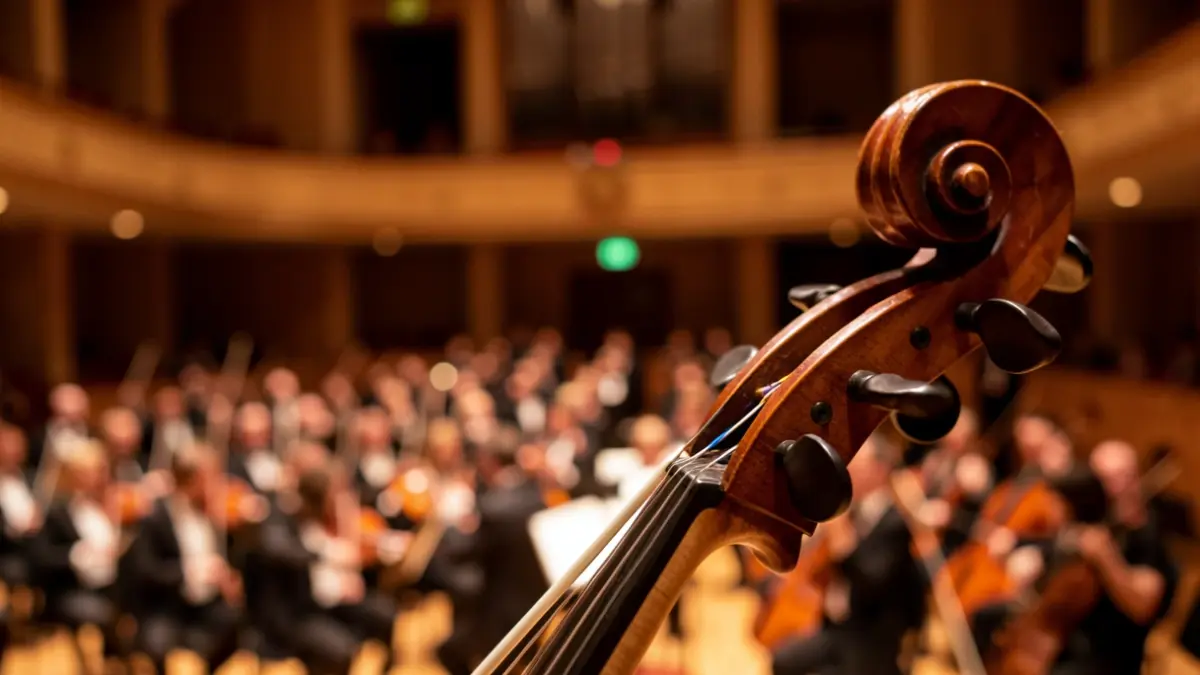 Primer plano del violonchelo con la orquesta y el teatro de fondo.