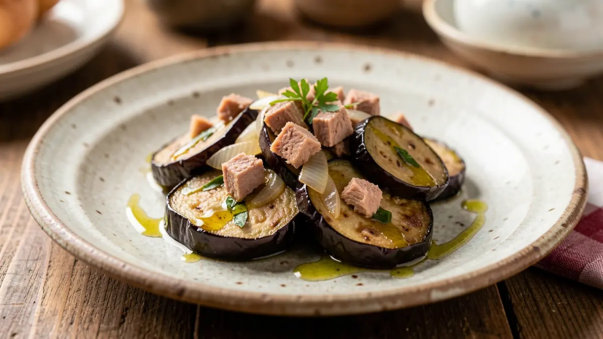 Plato de berenjena salteada con cebolla y atún, decorado con aceite de oliva.