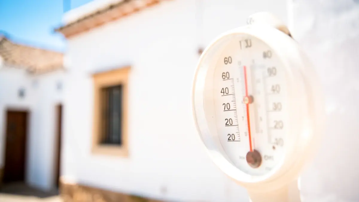 Thermometer showing high temperature with intense sun and white Andalusian facade in the background.