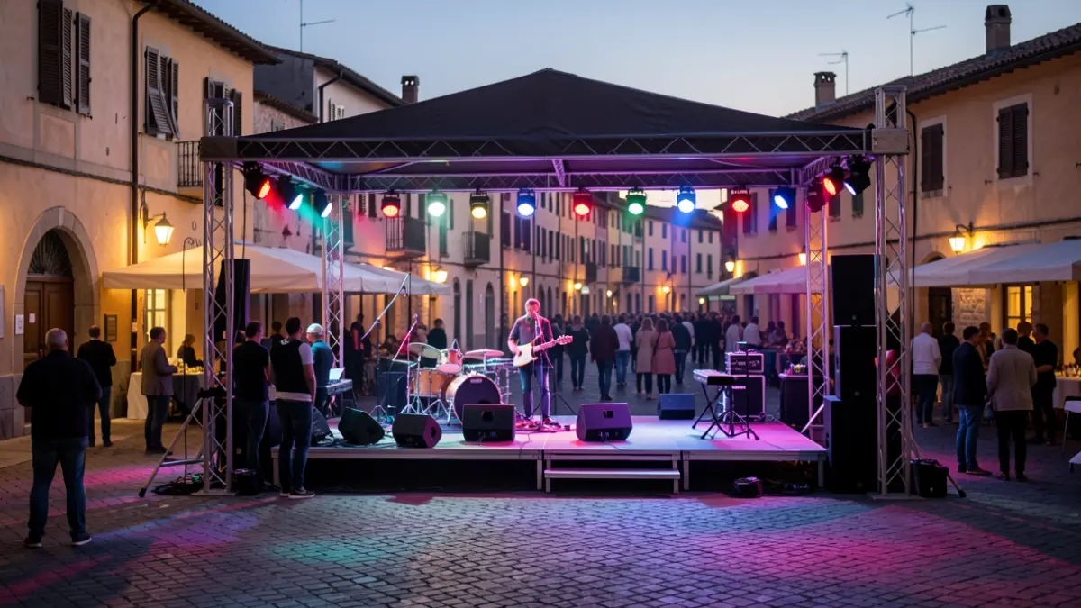Scene of an outdoor stage in a town square at dusk, with lights and a blurred audience.