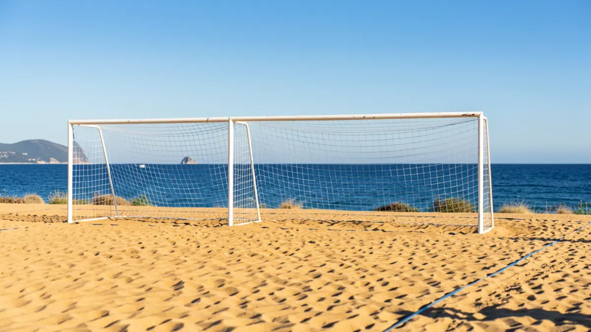 Campo de fútbol playa con porterías sobre arena dorada y el mar Mediterráneo al fondo.