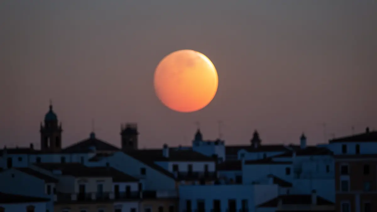 Eclipse solar parcial visto sobre el horizonte de una ciudad andaluza al atardecer.