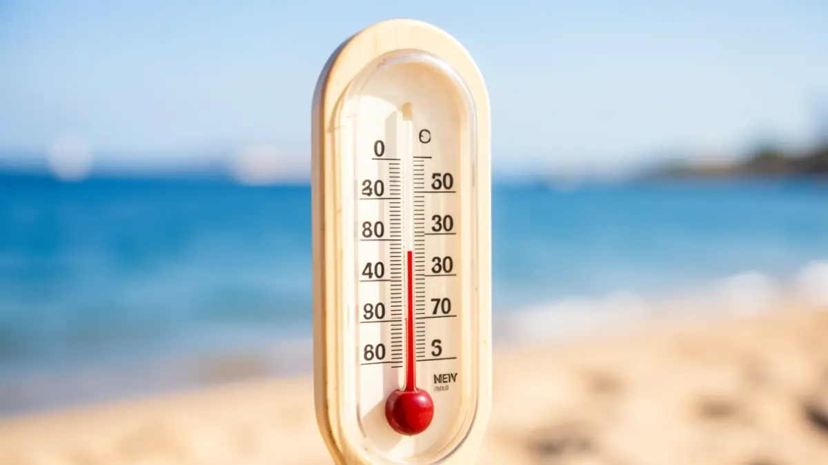 Thermometer showing high temperature with blurred beach water in the background.
