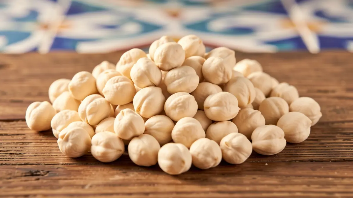 Chickpeas of the 'creamy white' variety from Campiña de Córdoba on a rustic wooden surface with Andalusian tile details.