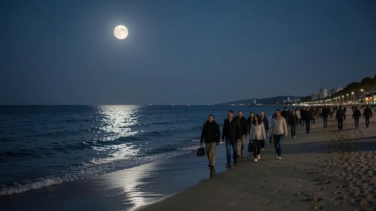 Imagen de personas caminando por la playa de noche bajo la luna llena.