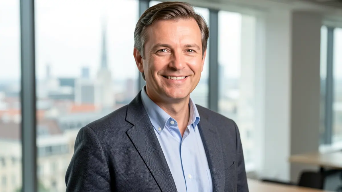 Image of a man with a kind demeanor in a modern office, with a blurred city in the background.